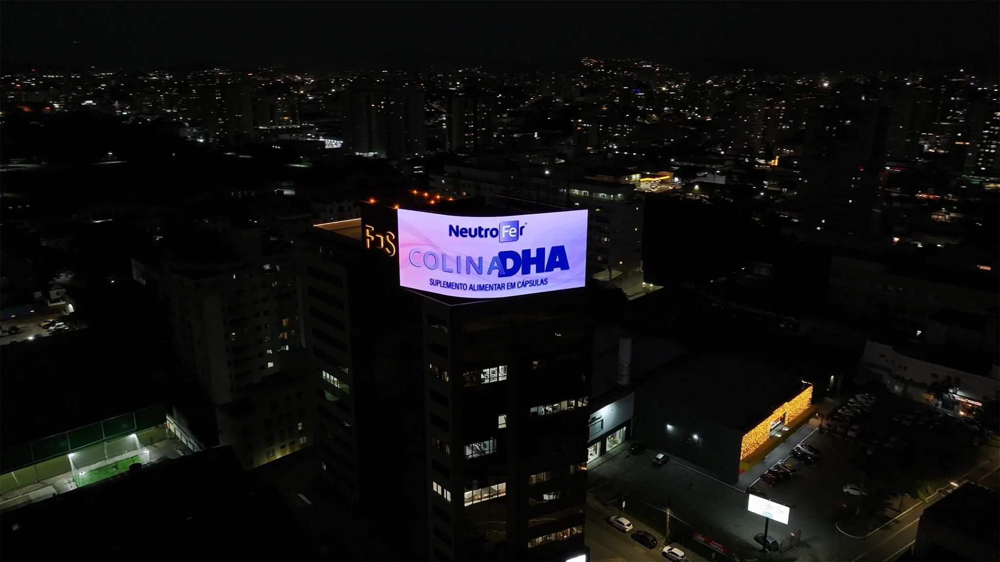 Megatela Floripa Square LED de 350m² em topo de prédio iluminada à noite com vista panorâmica para a Beira-mar Continental.